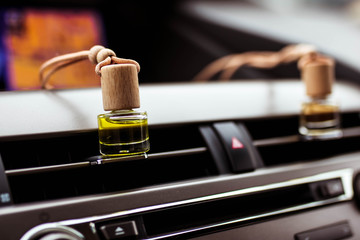 Car air perfume freshener bottles inside the car on car panel. Aromatic liquid in the small bottle.