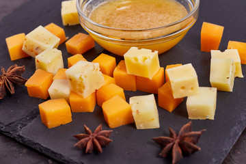 pieces of different cheese with honey on a stone plate