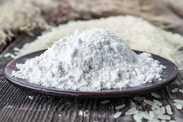 Rice flour in a bowl near the heap of white rice on old boards. Jasmine rice for cooking.