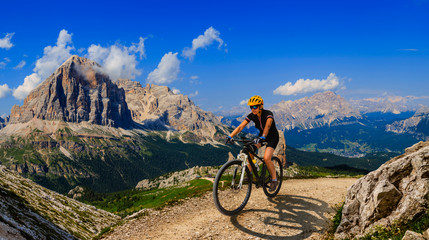 Tourist cycling in Cortina d'Ampezzo, stunning rocky mountains on the background. Woman riding MTB...