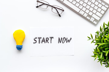 Start now. Motivative text on white office desk top-down