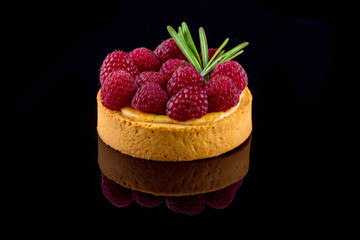  Small cake with raspberries on a black mirror surface. Close-up.