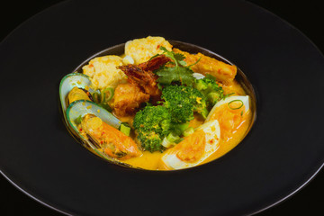 Freshly prepared seafood soup with vegetables and eggs. Black background.