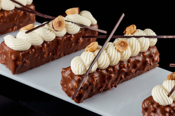  Chocolate-nut cakes decorated with cream, nuts and chocolate sticks on a white board. Black background.