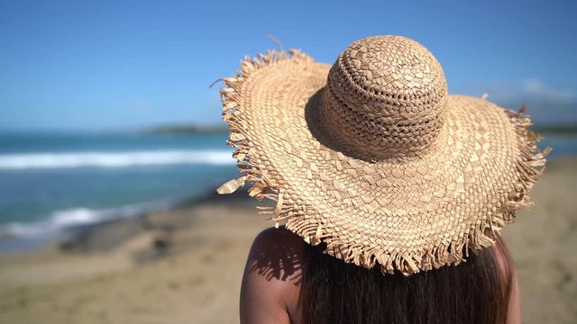 Woman relaxing on beach wearing sun hat fashion summer accessory. View from back of woman enjoying summer holidays.