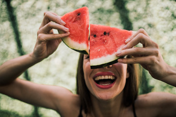 Woman holding dripping watermelon slices in front of face and laughing