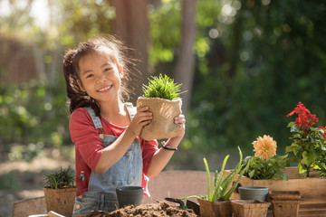 adorable asian little girl is planting spring flowers tree in pots in garden outside house, child...