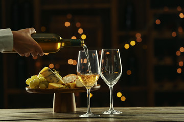 Waiter pouring delicious wine from bottle into glass on table in bar