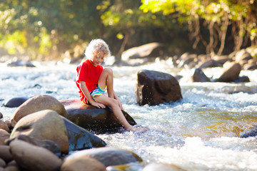 Child hiking in mountains. Kids at river shore.