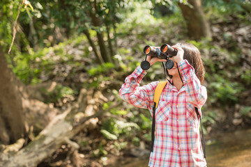 hiking women use binoculars to travel and have a happy smile. tourist looking through binoculars considers wild birds in the jungle. bird watching tours. with backpack. travel concept