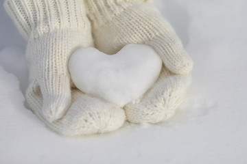 Fototapeta na wymiar Valentine day background. Female hands in knitted mittens with heart of snow in winter day. Love concept. 