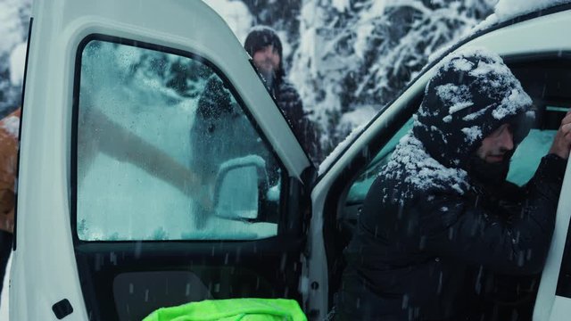 Car stuck in the snow on the road, the man and his friends trying to get him out. Transportation concept.