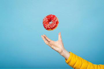 Hand catch a donut with red icing. Blue cardboard background. The concept of baking, handmade. Flat...