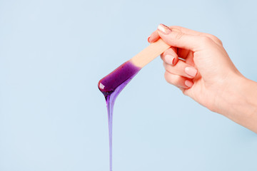 depilation and beauty concept - sugar paste or wax honey for hair removing with wooden waxing spatula sticks in hand on blue background, copy space, beauty industry, concept of smooth skin remove - 322258941