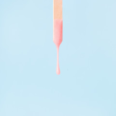 liquid pink wax or sugar paste for depilation drains from the stick on blue background. The concept...