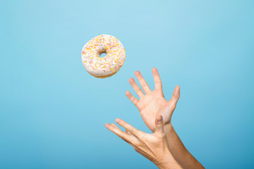 Hands catch a donut with icing. Blue cardboard background. Concept of baking, handmade. Flat lay,...