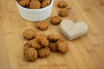 Very tasty peanut butter biscuits on bamboo wooden board in white baking bowl and decorative wood heart, golden baked healthy