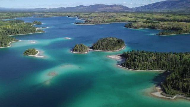 Flying over the beautiful small islands of Boya Lake in Canada with mountains in the distance - Aerial shot