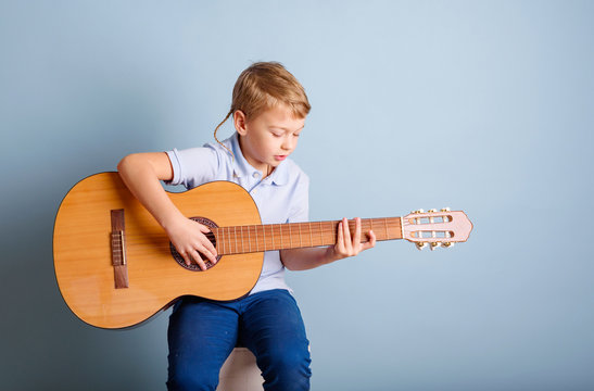 cute blond boy playing guitar on a blue background, the concept of learning to play guitar - Powered by Adobe