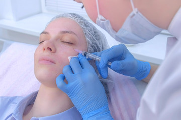 Cosmetologist doctor making multiple injections biorevitalization in woman face skin under eye, portrait closeup. Mesotherapy and face lifting in beauty clinic. Beautician's hands and girl's face.