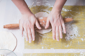 Women's hands in flour roll out the dough on the table with a rolling pin close-up, the table is sprinkled with flour