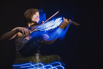 A woman plays the violin on the background of abstract light strips, visualization of musical...