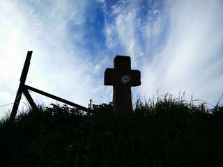 Cross burialstone silhouette in meadow with great sky