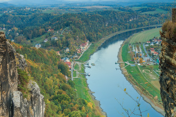 Fototapeta na wymiar View of the Elbe valley from the Bastei bridge in the evening. View of the spa town of Rathen. Rocks and trees in autumn. Buildings, ship and ferry on the river