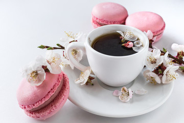Pink macaroons with a cup of coffee and a branch of white flowers on a white background. French...