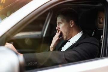 young businessman looks tired yawning while siting in his car with open window, safety driving concept