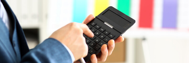 Male arm in suit hold calculator pressing buttons in office closeup. Electronic keypad math data...