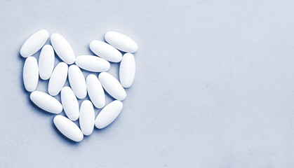 heart shaped medical white oval pills isolated on blue background.