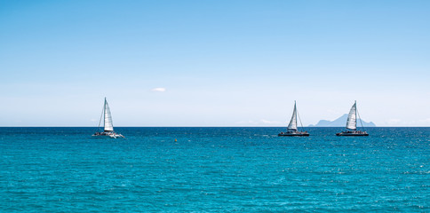 Panoramic sea view with three sailing boats cruising on the ocean.