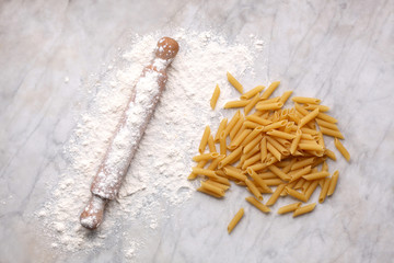 uncooked pasta, rolling pin and flour rest on a marble table with copy space for your text