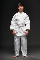 a teenager dressed in martial arts clothing poses on a dark gray background, a sports concept