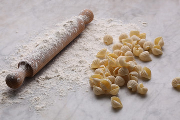 uncooked pasta, rolling pin and flour rest on a marble table with copy space for your text