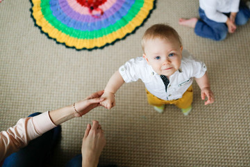 Baby boy stands leaning on his mother's hand