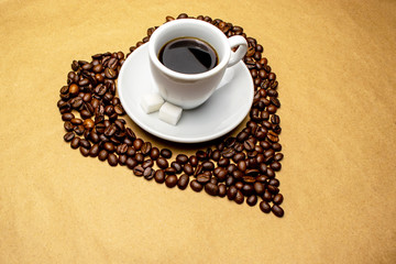 white cup with coffee in the center of the heart made from coffee beans on a beige background