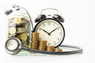 conceptual money growing, increasing finance situations, time cost money. stacked money coins, stethoscope, clock and a glass bottle of coins againt white background . free copy space for your text
