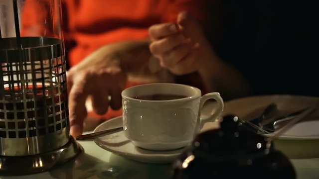 closeup of hot steaming tea in a white tea glass on a tea party with female hands gesticulation in worm semidarkness lighting