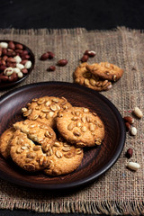 Homemade peanut cookies on a brown plate with raw peanuts in background
