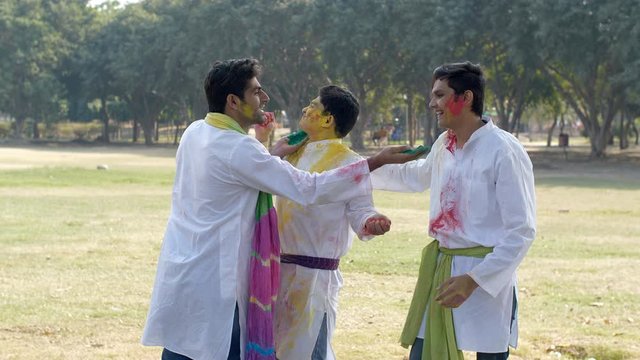 Young friends in traditional clothing celebrating Holi festival together in a park. A group of Indian teenagers happily enjoying and coloring each other with organic Gulal colors during Holi celebr...