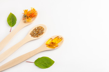 Herbal capsule, natural vitamins, dry calendula flowers at wooden spoon on white background....