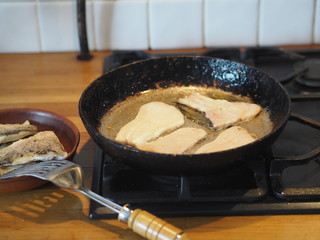Home cooking. Fry river fish with pike slices in a black pan on a gas stove. Prepare the filling for the pie.
