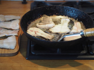 Home cooking. Fry river fish with pike slices in a black pan on a gas stove. Prepare the filling for the pie.