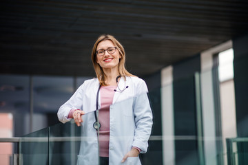 Portrait of female doctor standing on corridor, looking at camera.