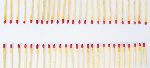Two row's of red wooden match sticks facing each other on a white background