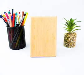 Wooden plaque with a pencil holder full of crayons and a miniature tree on a white background