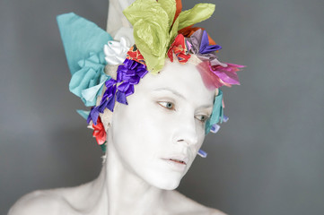 Exotic unusual white clay face woman makeup with floral headwear