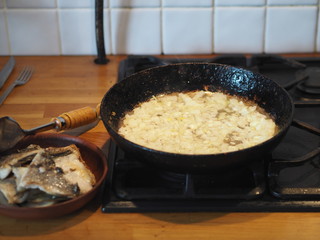 Home cooking. Fried onions in oil in a black pan on the stove. Nearby fried fish. The stage of preparation of the filling for the pie.